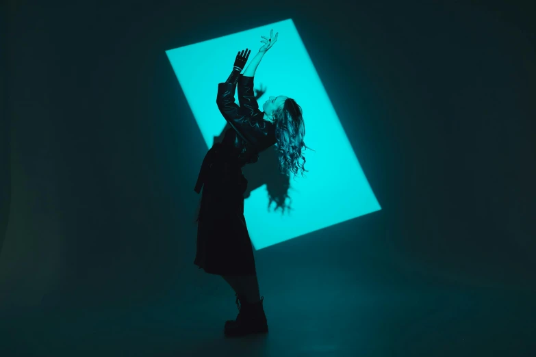 a woman standing in front of a blue light, an album cover, unsplash, conceptual art, dramatic floating pose, square, black and cyan color scheme, grimes