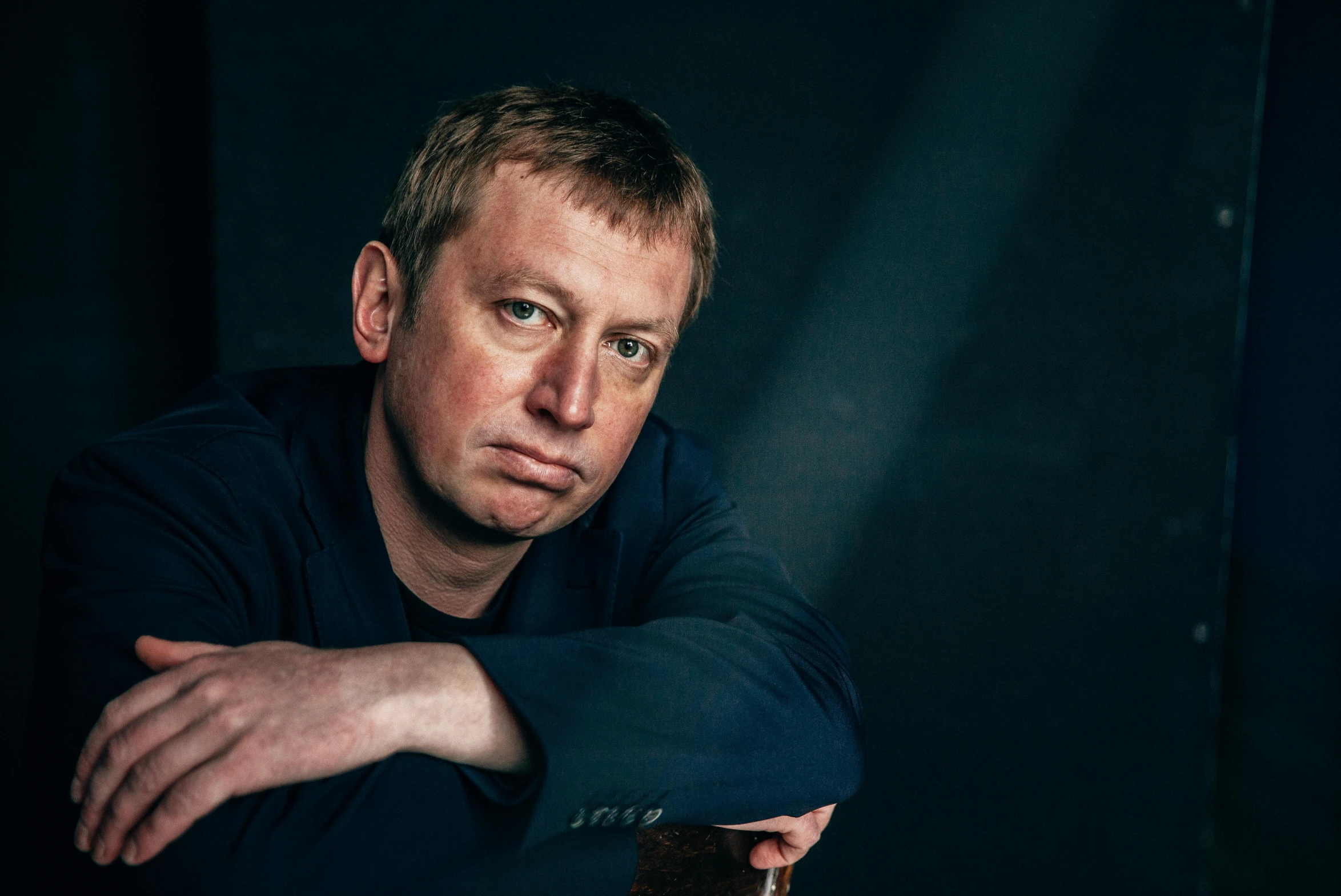 a man sitting at a table with a glass of wine, an album cover, inspired by Jan Rustem, unsplash, photorealism, simon pegg portrait, mark e smith, ( low key light ), limmy