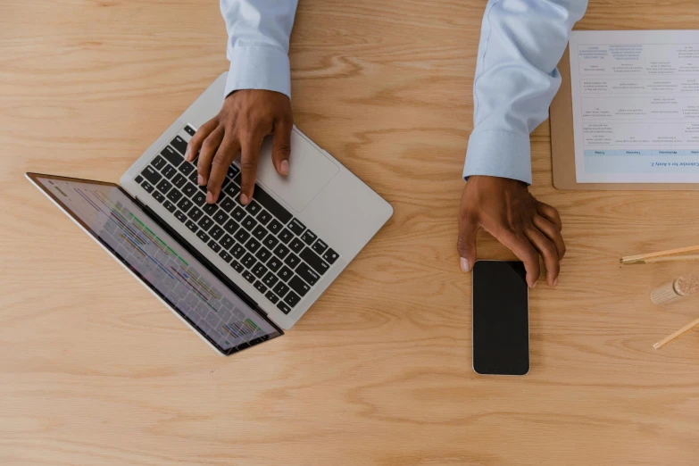 a man sitting at a desk using a laptop computer, trending on pexels, top-down shot, holding a very advance phone, standing on a desk, thumbnail