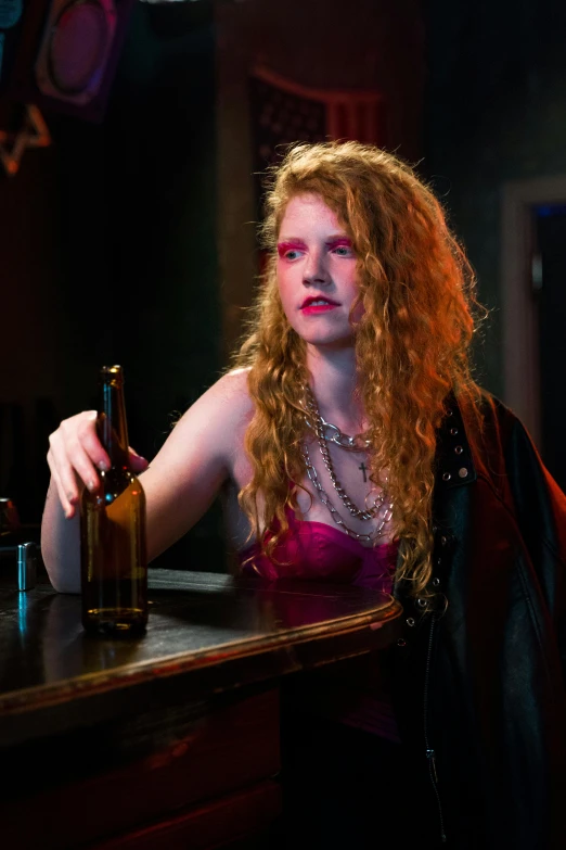 a woman sitting at a bar with a bottle of beer, a portrait, inspired by Nan Goldin, pexels, renaissance, wild ginger hair, black canary, production still, [ theatrical ]