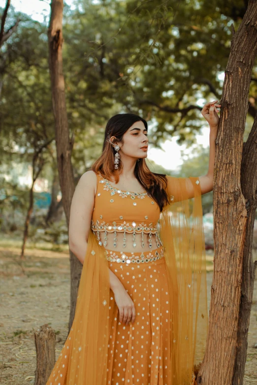 a woman standing next to a tree in a yellow dress, inspired by Saurabh Jethani, pexels, wearing an ornate outfit, wearing crop top, embellished sequined, thicc