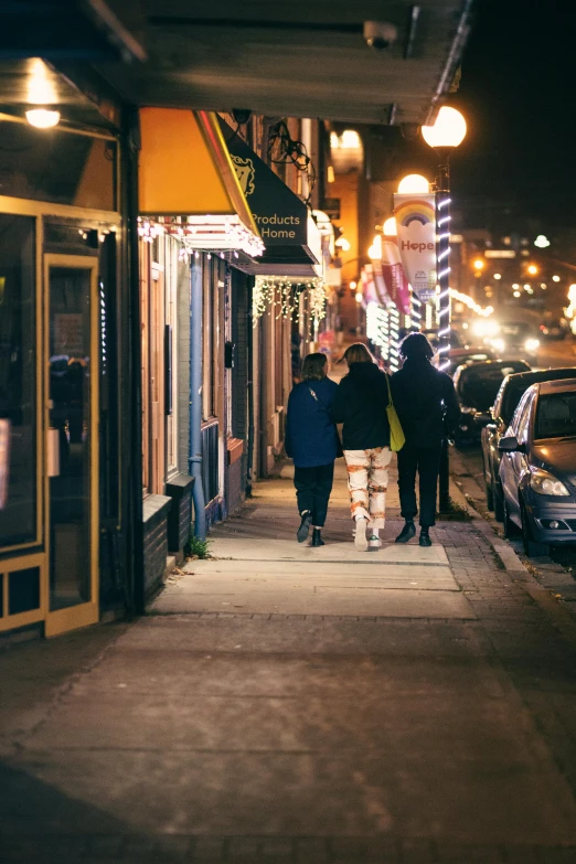 a group of people walking down a street at night, midwest town, warm street lights store front, cozy lights, february)