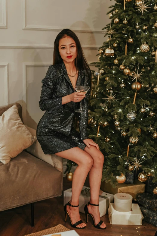 a woman sitting on a couch next to a christmas tree, a portrait, by Julia Pishtar, reddit, wearing a cocktail dress, wearing a full leather outfit, asian women, enjoying a glass of wine