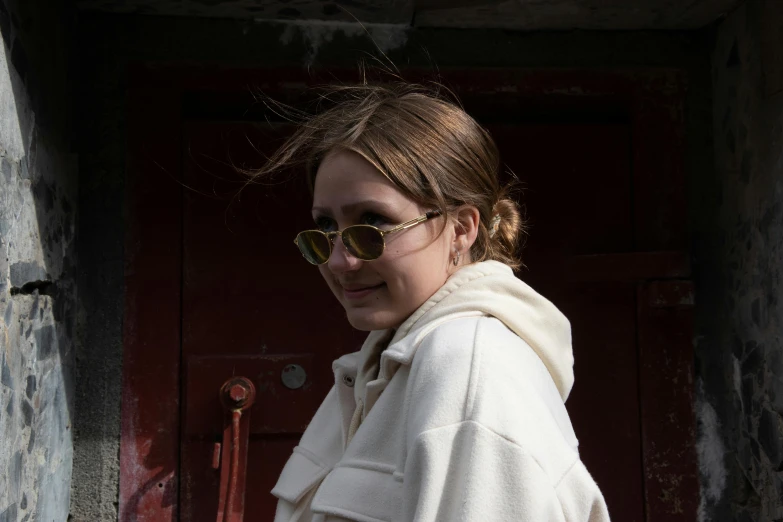 a woman standing in front of a red door, inspired by Elsa Bleda, trending on pexels, happening, reflective aviator sunglasses, beautiful taissa farmiga, wearing a white winter coat, profile pic