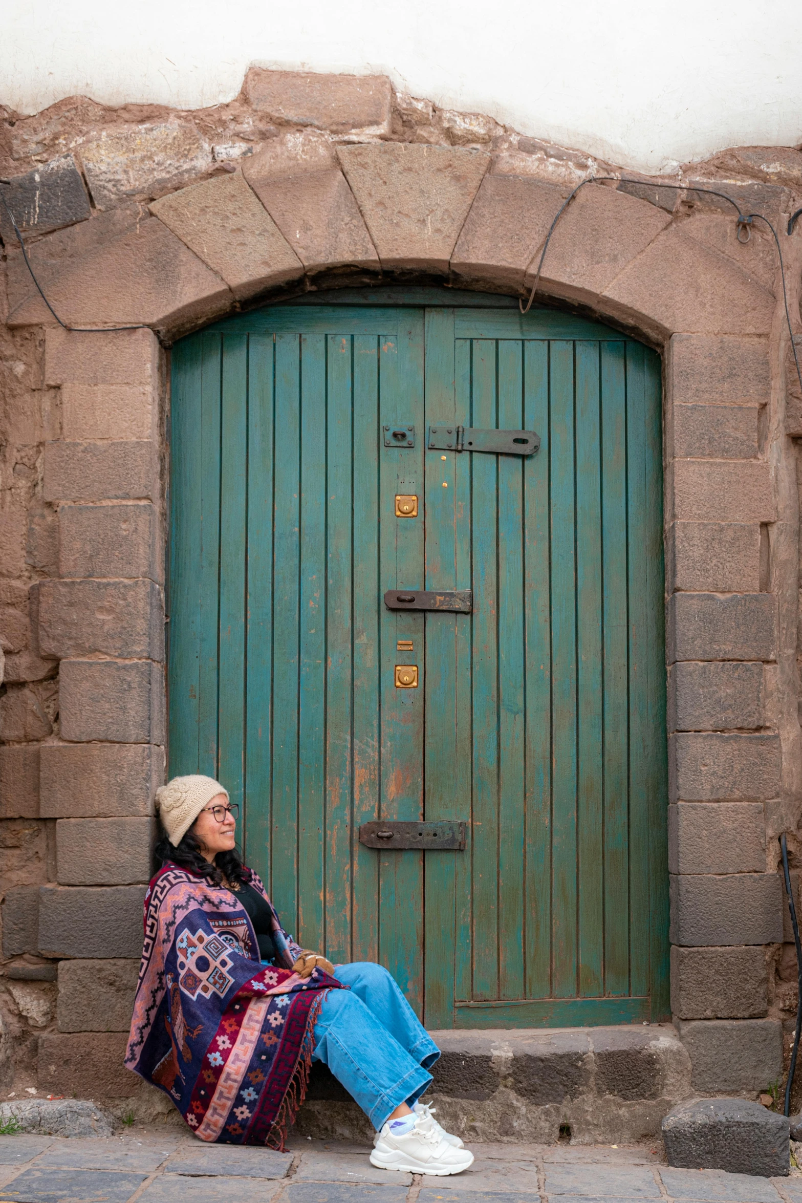 a woman sitting in front of a green door, inspired by Osman Hamdi Bey, unsplash, quechua, neo - andean architecture, brown, freezing