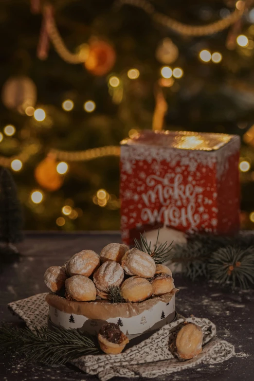 a box of cookies sitting on top of a table next to a christmas tree, a still life, by Julia Pishtar, natural candle lighting, thumbnail, rim lights wlop, good morning
