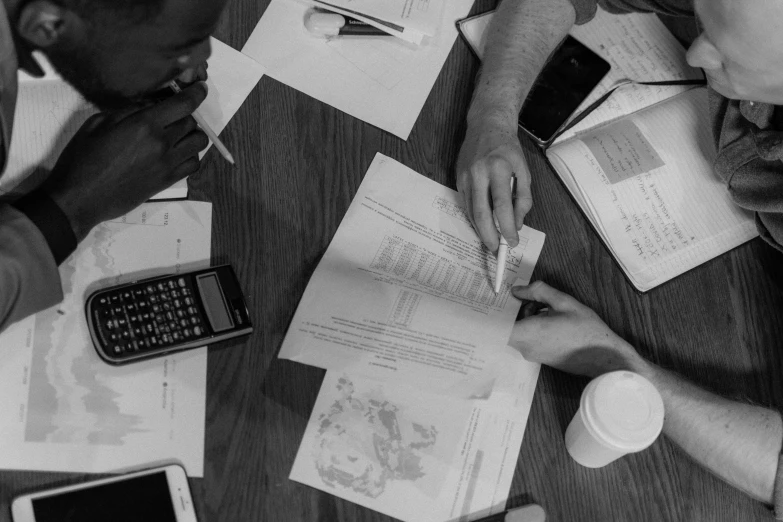 a group of people sitting around a wooden table, by Matt Cavotta, piles of paperwork, black and white coloring, formulas, phone photo