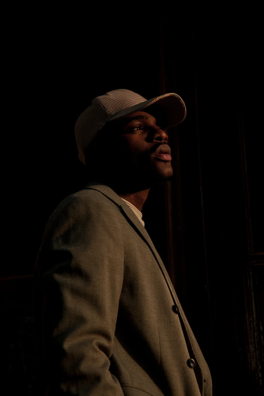 a man in a suit and hat standing in a dark room, ( ( dark skin ) ), profile pic, ( ( theatrical ) ), warmly lit