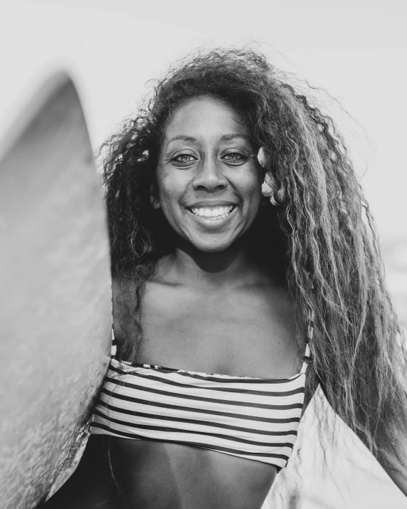 a black and white photo of a woman holding a surfboard, by Olivia Peguero, long afro hair, happily smiling at the camera, portrait of maci holloway, wavy hair spread out