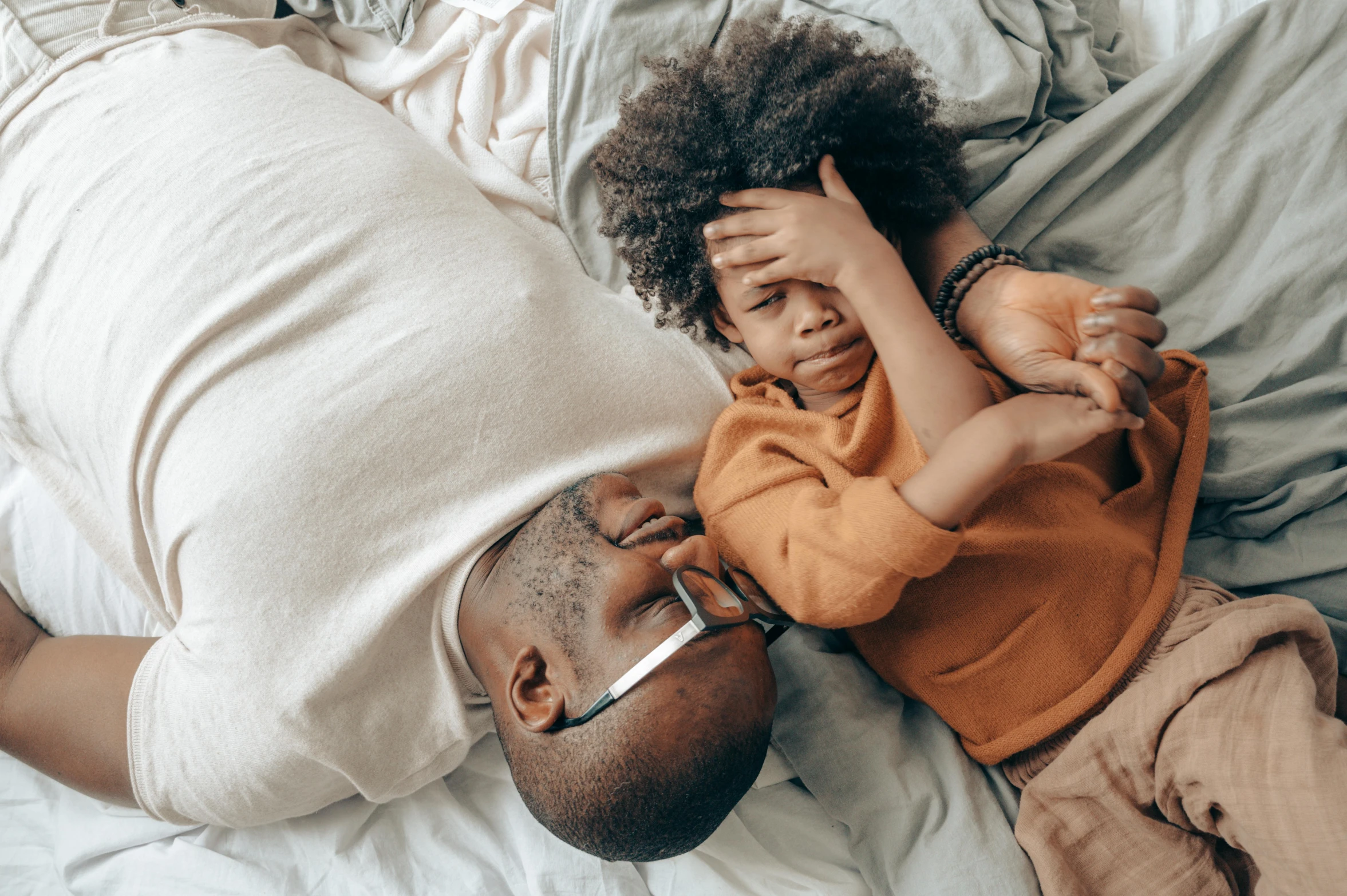 a man laying on top of a bed next to a child, pexels contest winner, curls on top of his head, african american, sympathetic, bedhead