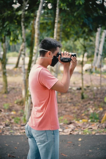a man taking a picture with a camera, wearing facemask, in the tropical wood, ground camera, photography]