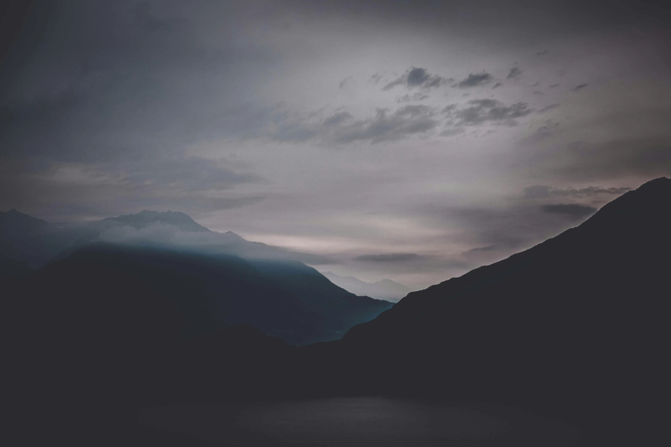 a body of water surrounded by mountains under a cloudy sky, a picture, unsplash contest winner, minimalism, ominous night mist, silhouetted, multiple stories, faded colours