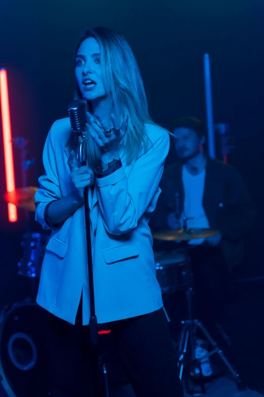 a woman that is standing in front of a microphone, an album cover, pexels, blue light accents, band playing, blonde, ( ( theatrical ) )