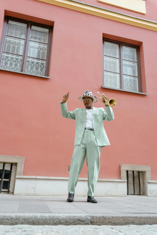 a man that is standing in front of a building, an album cover, by Ottó Baditz, pexels contest winner, harlem renaissance, court jester, brass horns, sea - green and white clothes, budapest