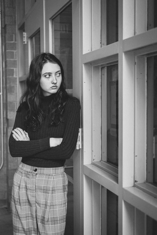 a black and white photo of a woman leaning against a window, inspired by Diane Arbus, pexels contest winner, realism, maisie williams, annoyed, portrait of high school girl, stood in a cell