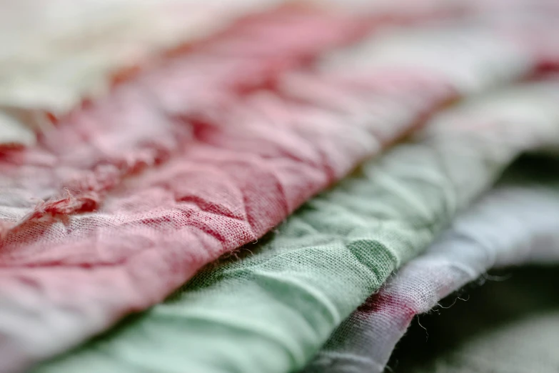 a pile of fabric sitting on top of a table, by Sylvia Wishart, unsplash, pink white and green, using the degrade technique, detail shot, olive green and venetian red