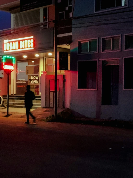 a person walking down a street at night, by Alejandro Obregón, storefronts, in an american suburb, promo image, bixbite