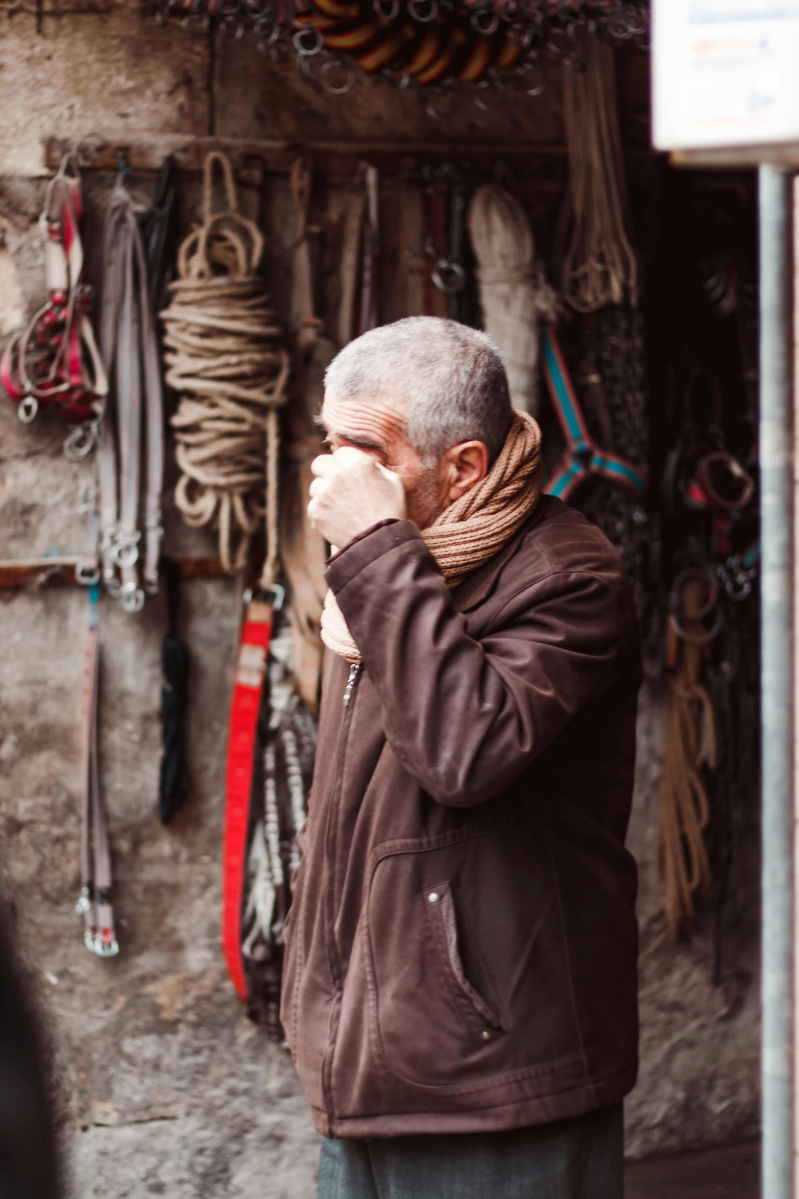 a man standing in front of a store talking on a cell phone, sick with a cold, damascus, portrait featured on unsplash, brown clothes