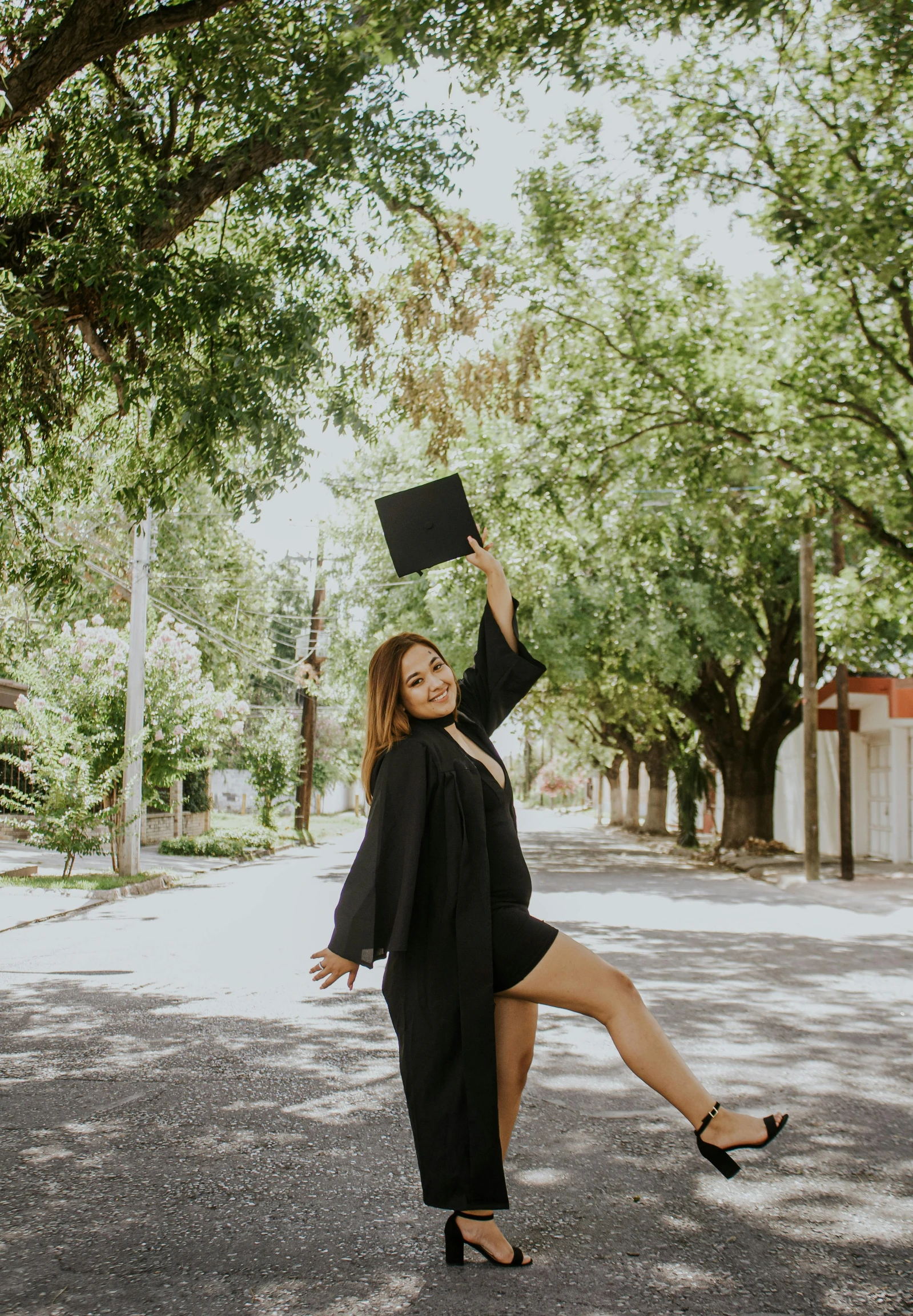 a woman standing in the middle of a road holding a book, an album cover, unsplash, academic art, wearing an academic gown, doing a sassy pose, wearing black clothes, waving and smiling