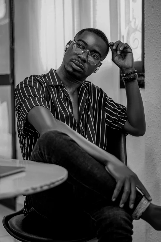 a man sitting on a chair in front of a laptop, a black and white photo, by Clifford Ellis, pexels contest winner, realism, adebanji alade, androgynous person, with glasses on, 21 years old