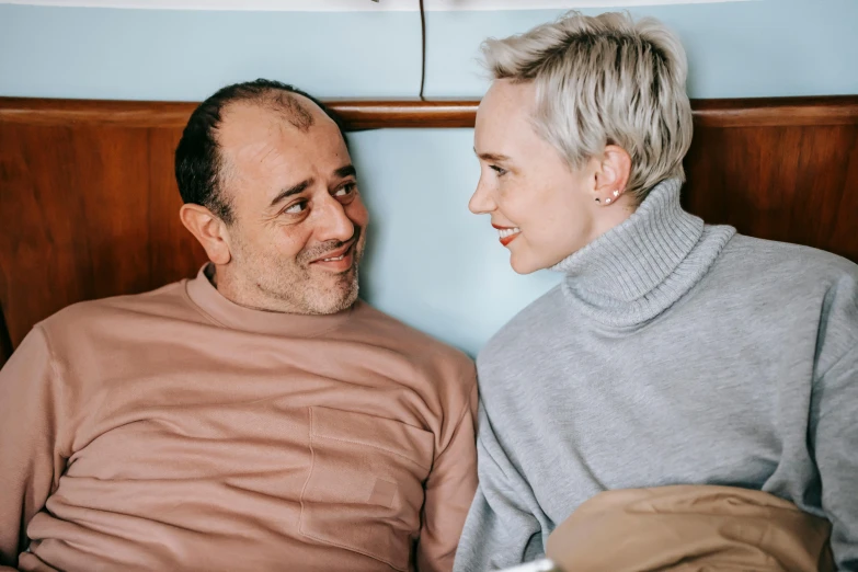 a man and woman sitting next to each other on a bed, trending on pexels, antipodeans, buzz cut gray hair, in hospital bed, non binary model, smiling at each other