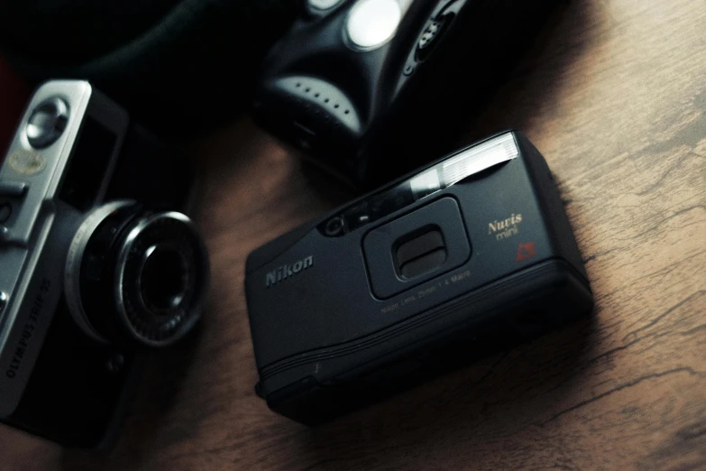 a couple of cameras sitting on top of a wooden table, a picture, shot on nicon camera, vhs colour photography, dark-toned product photos, photograph taken in 2 0 2 0