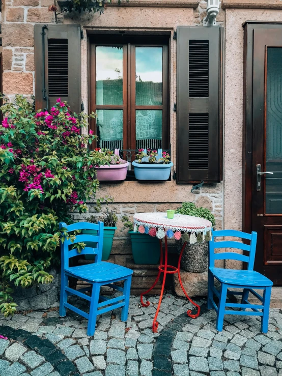 a couple of blue chairs sitting on top of a cobblestone street, by Anna Haifisch, pexels contest winner, arts and crafts movement, with colorful flowers and plants, cafe, 🚿🗝📝, youtube thumbnail