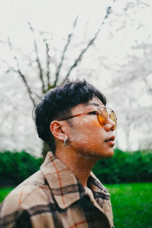 a man wearing glasses standing in front of a tree, an album cover, inspired by Joong Keun Lee, trending on pexels, non-binary, rainy outside, profile image, sunfaded