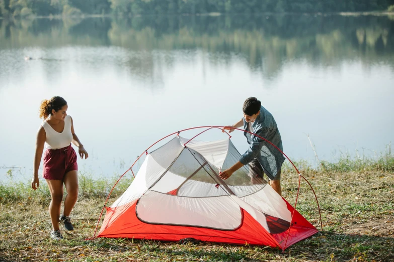 a man and woman setting up a tent next to a lake, pexels contest winner, red and white color theme, full product shot, rectangle, back facing