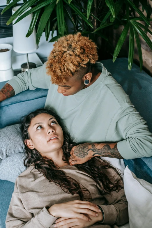 a man sitting next to a woman on a couch, a tattoo, trending on pexels, renaissance, laying in bed, mixed-race woman, comforting, lesbian