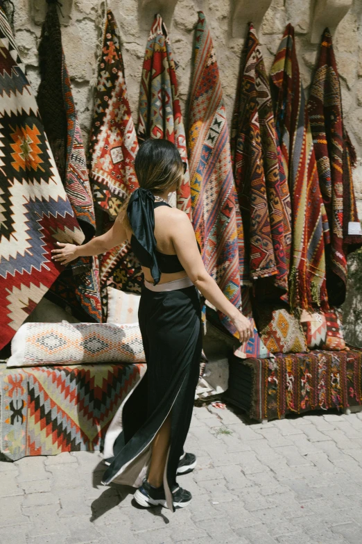 a woman standing in front of a display of rugs, by Julia Pishtar, trending on unsplash, ancient city streets behind her, sarong, inspect in inventory image, in the sun