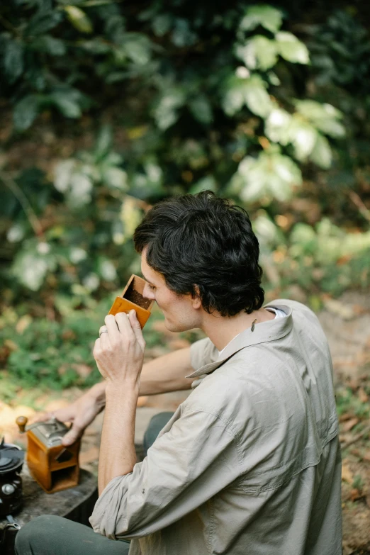 a man sitting at a picnic table eating food, by Jessie Algie, pexels contest winner, in a jungle, attractive man drinking coffee, avatar image, holding a wood piece