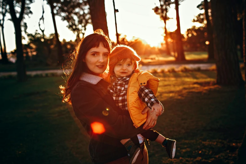 a woman holding a child in a park, by Julia Pishtar, pexels contest winner, golden hour 8k, handsome, avatar image, warm orange lighting