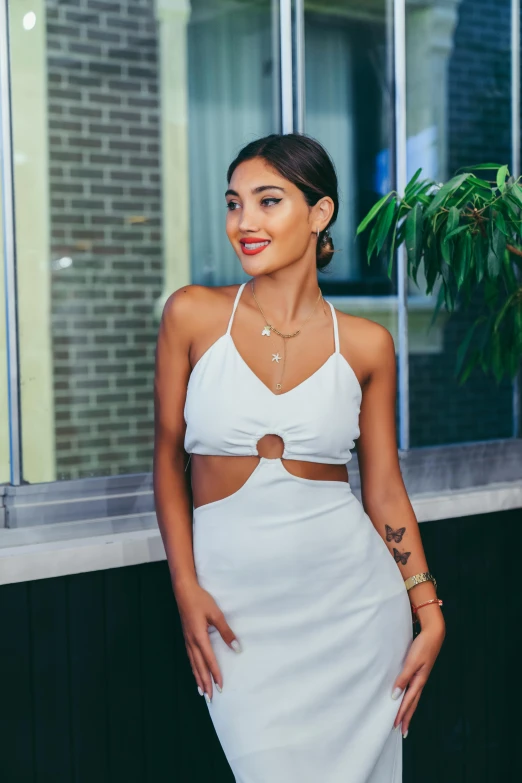 a woman standing in front of a window wearing a white dress, by Robbie Trevino, wearing a crop top, mia khalifa, chrome outfit, feature