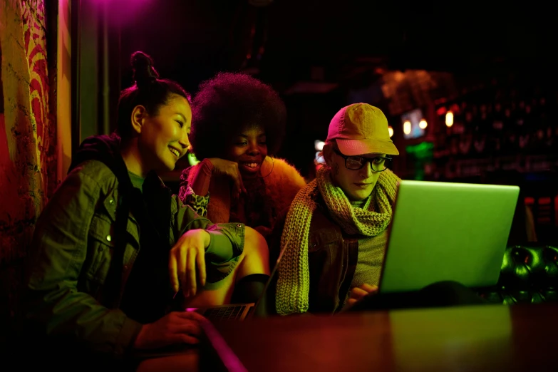 a group of people sitting at a table with a laptop, by Joe Bowler, pexels, happening, night clubs and neons, avatar image, blank, playful smirk