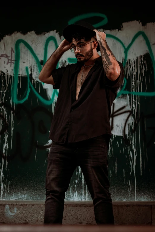 a man standing in front of a graffiti covered wall, an album cover, inspired by Byron Galvez, pexels contest winner, with a beard and a black shirt, doing a hot majestic pose, zayn malik, rain lit