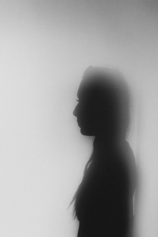 a woman standing in front of a white wall, a black and white photo, by Zsolt Bodoni, silhouetted, volumetric haze, headshot profile picture, (((mist)))
