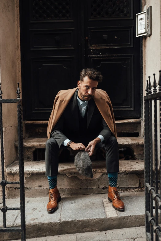 a man sitting on the steps of a building, trench coat and suit, curated collections, about to step on you, wearing a barca cape