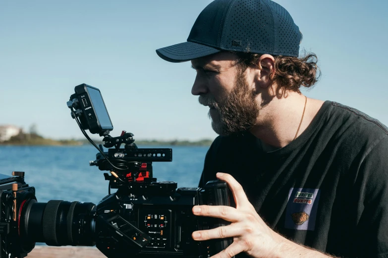 a man holding a camera next to a body of water, red cinema camera, avatar image