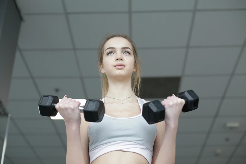 a beautiful young woman lifting weights in a gym, a picture, pexels contest winner, renaissance, portrait sophie mudd, plain background, teenager girl, mid 2 0's female