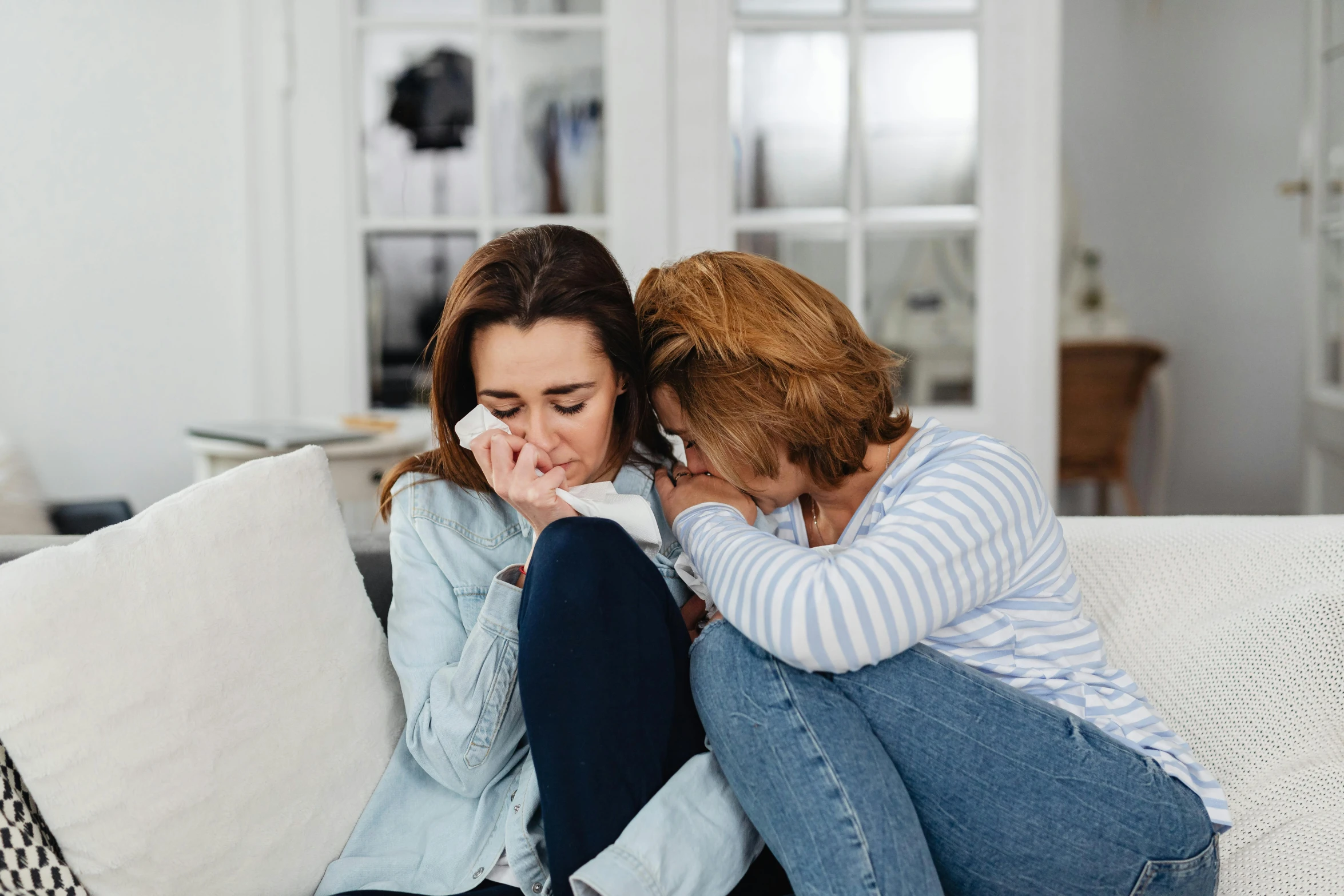 a couple of women sitting on top of a couch, pexels, crying one single tear, mourning family, instagram post, hugging her knees