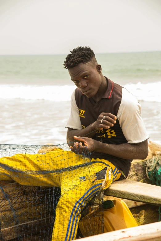 a man sitting on top of a boat next to the ocean, intricate african jewellery, netting, male teenager, biopic