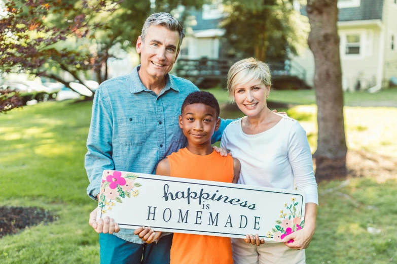 a family holding a sign that says happiness is homemade, by John Backderf, pexels, happening, avatar image, mid length portrait photograph, romantic lead, catalog photo