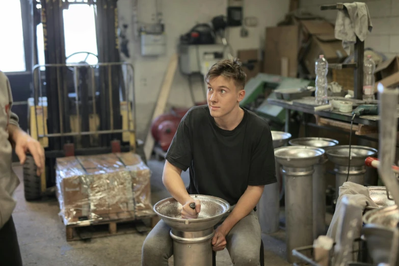 a man sitting on top of a metal bowl, by Thomas Furlong, process art, stood in a factory, slightly smiling, pouring, liam brazier