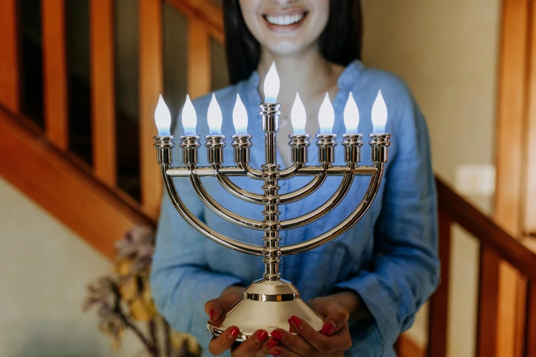 a woman holding a menorah with candles on it, leds, brass plated, 💣 💥💣 💥, light skin