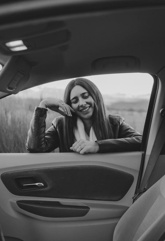 a woman sitting in the passenger seat of a car, a black and white photo, pexels contest winner, leaning on door, happy girl, album cover, avatar image