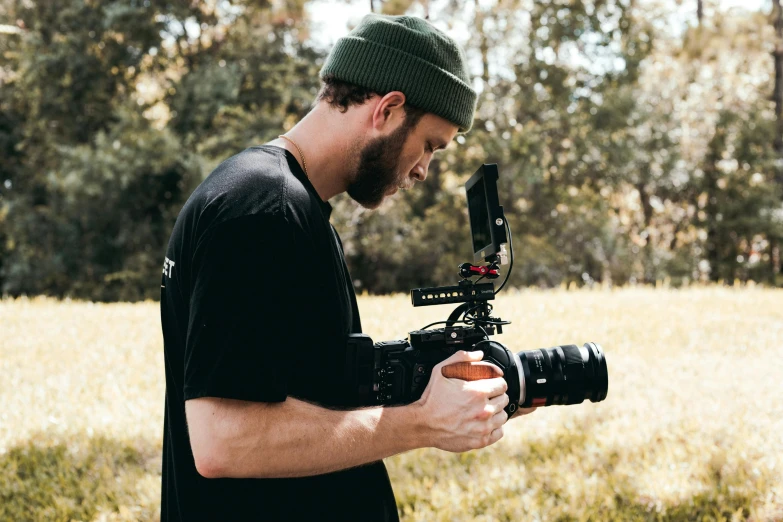 a man standing in a field holding a camera, red cinema camera, lachlan bailey, **cinematic, performing a music video