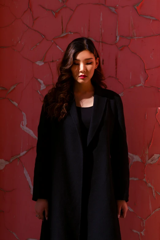 a woman standing in front of a red wall, inspired by Xia Chang, wearing black overcoat, plain background, met collection, gongbi