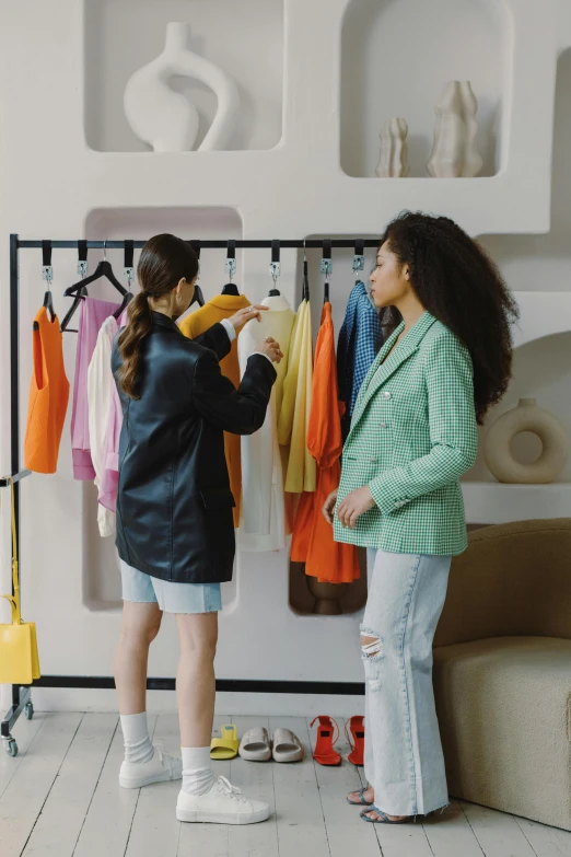 a couple of women standing next to each other in a room, trending on pexels, people shopping, orange jacket, talking, thumbnail