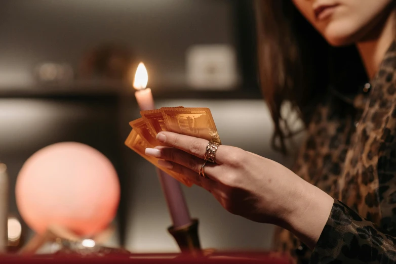 a woman lighting a candle on a table, by Julia Pishtar, trending on pexels, wizard shuffling cards, warm orange lighting, profile image, fan favorite